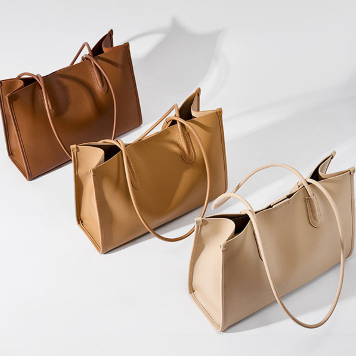 Pair of leather tote bags with long handles in warm brown and cream tones